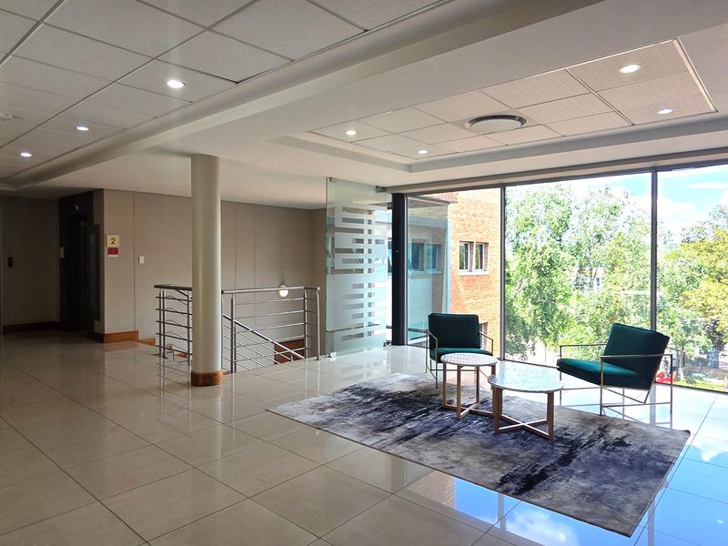 Modern office lobby area featuring polished tile floors, suspended ceilings with recessed lighting, and large floor-to-ceiling windows providing ample natural light.