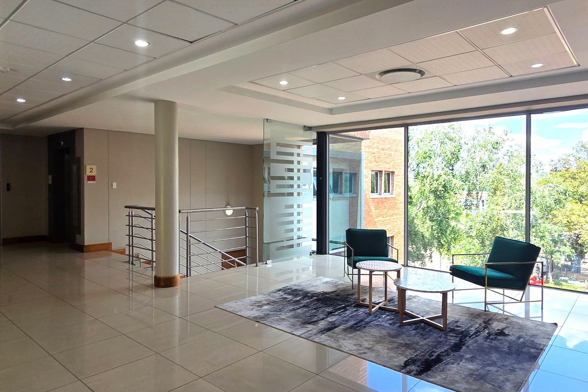 Modern office lobby area featuring polished tile floors, suspended ceilings with recessed lighting, and large floor-to-ceiling windows providing ample natural light.