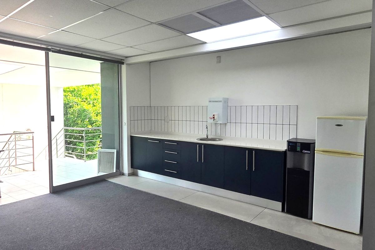 A functional office kitchenette featuring dark cabinetry, a sink, tiled backsplash, and direct access to an outdoor balcony area.