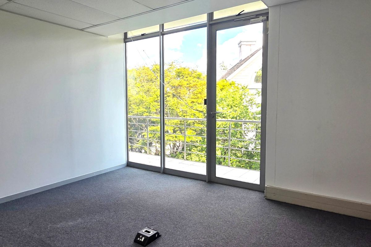 A bright, empty office space featuring a suspended ceiling, carpeted flooring, and large glass doors leading to a private balcony.