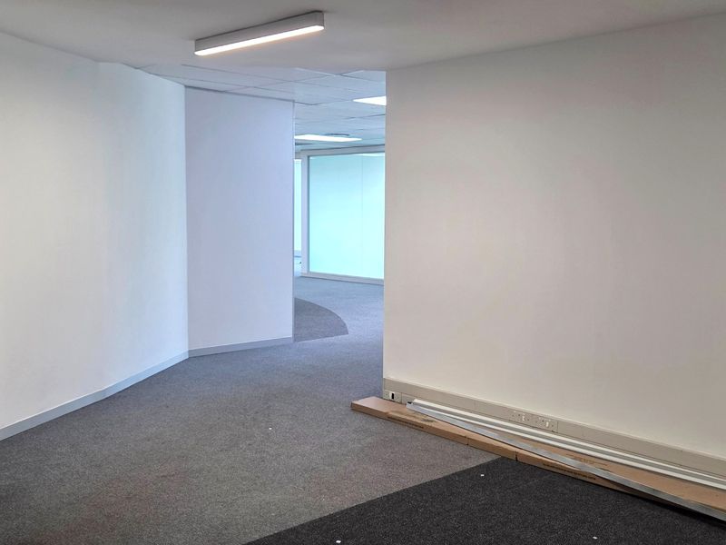 An empty, open-plan office space featuring neutral carpeting, recessed lighting, and glass partitions, providing a clean and versatile professional work environment.