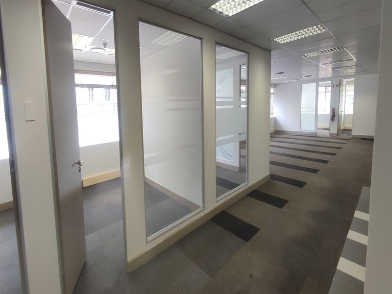An open-plan office space featuring glass-partitioned private offices, suspended ceilings with recessed lighting, and durable carpet tile flooring.