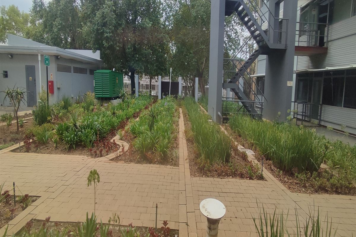 A well-maintained rear courtyard area featuring paved walkways, landscaped garden beds, and an external metal staircase providing access to the office building.