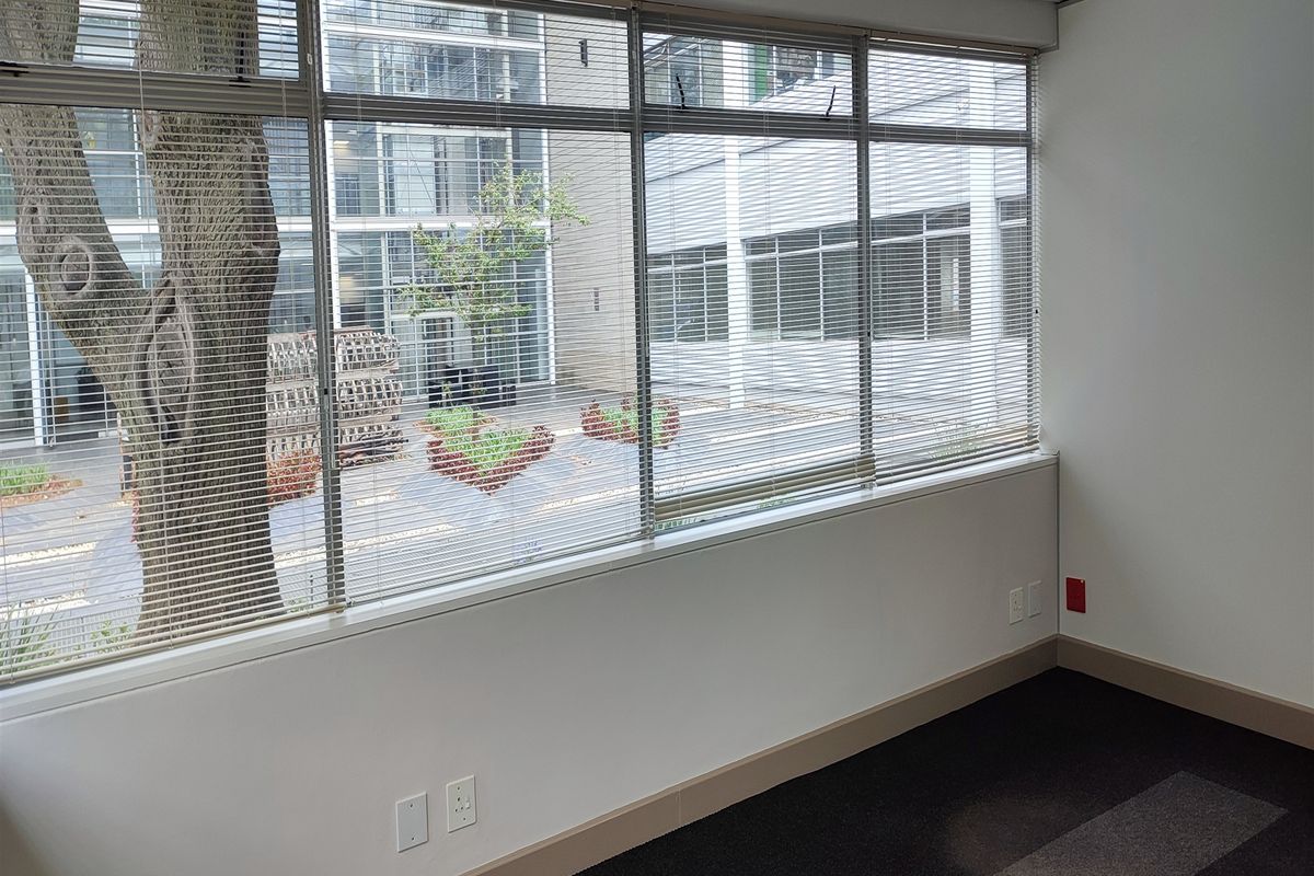 A bright, empty office space featuring large windows with venetian blinds, carpeted flooring, and integrated electrical and data connectivity.