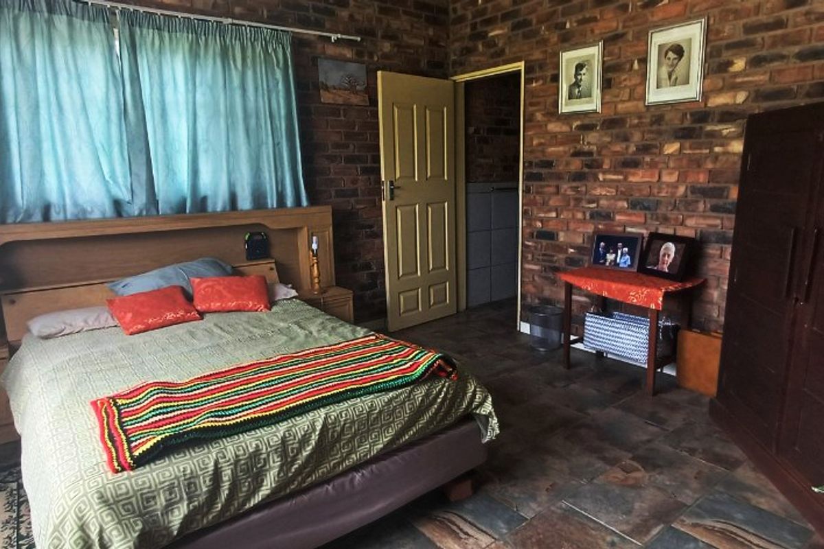 A rustic bedroom featuring exposed brick walls, slate tile flooring, and a built-in headboard, offering a traditional farm-style aesthetic.