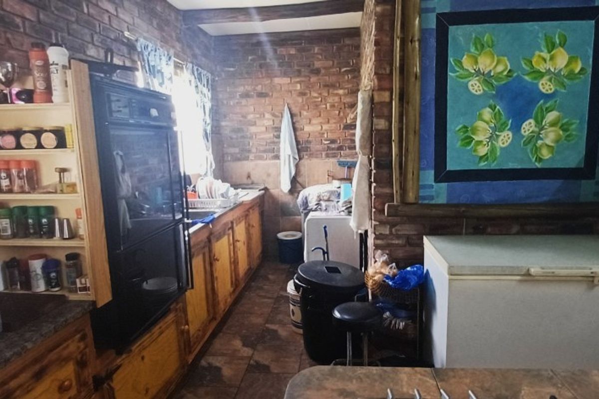 A rustic kitchen featuring exposed brick walls, wooden cabinetry, and tiled flooring, offering a traditional farm-style aesthetic in need of modernization.