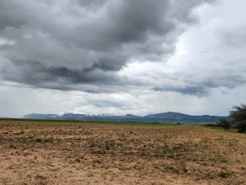 Expansive view of open farmland under a cloudy sky with distant mountain ranges on the horizon.