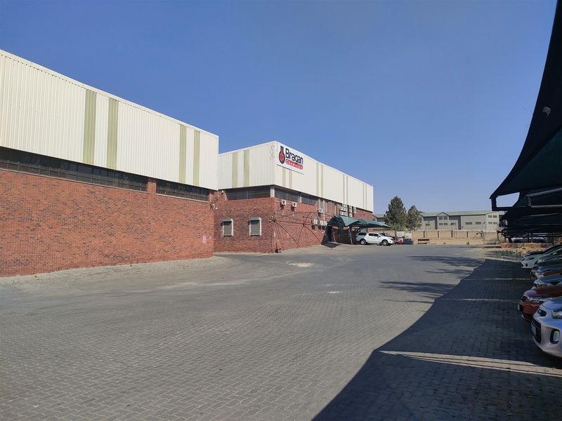 Industrial property featuring a brick and metal facade with a large paved driveway and covered parking area.