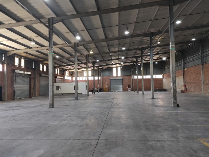 Spacious industrial warehouse featuring high ceilings, concrete flooring, multiple roller shutter doors, and an internal office pod, suitable for various commercial or storage operations.