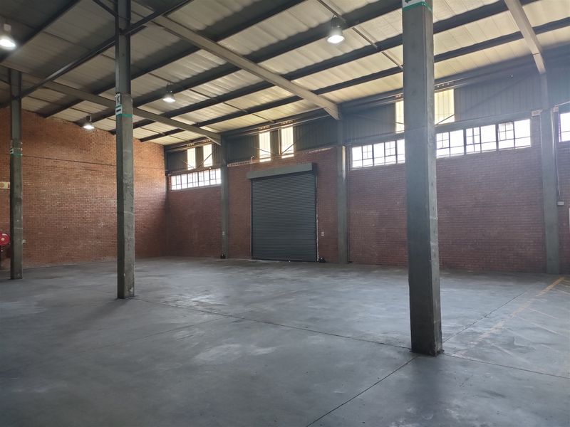 Spacious industrial warehouse unit featuring exposed brick walls, concrete flooring, high ceilings with steel portal frame, and a large roller shutter door.