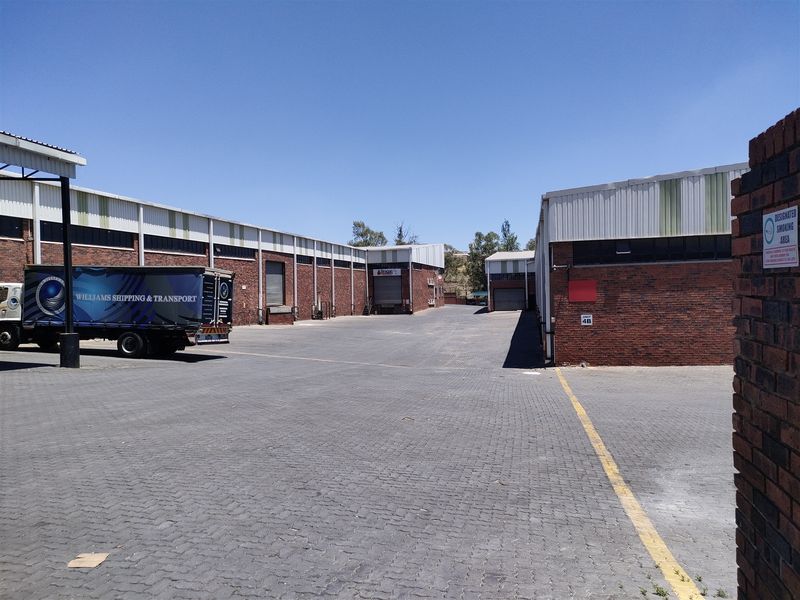 Spacious industrial yard area featuring paved surfaces, multiple roller shutter access points, and brick-clad warehouse structures suitable for logistics and transport operations.