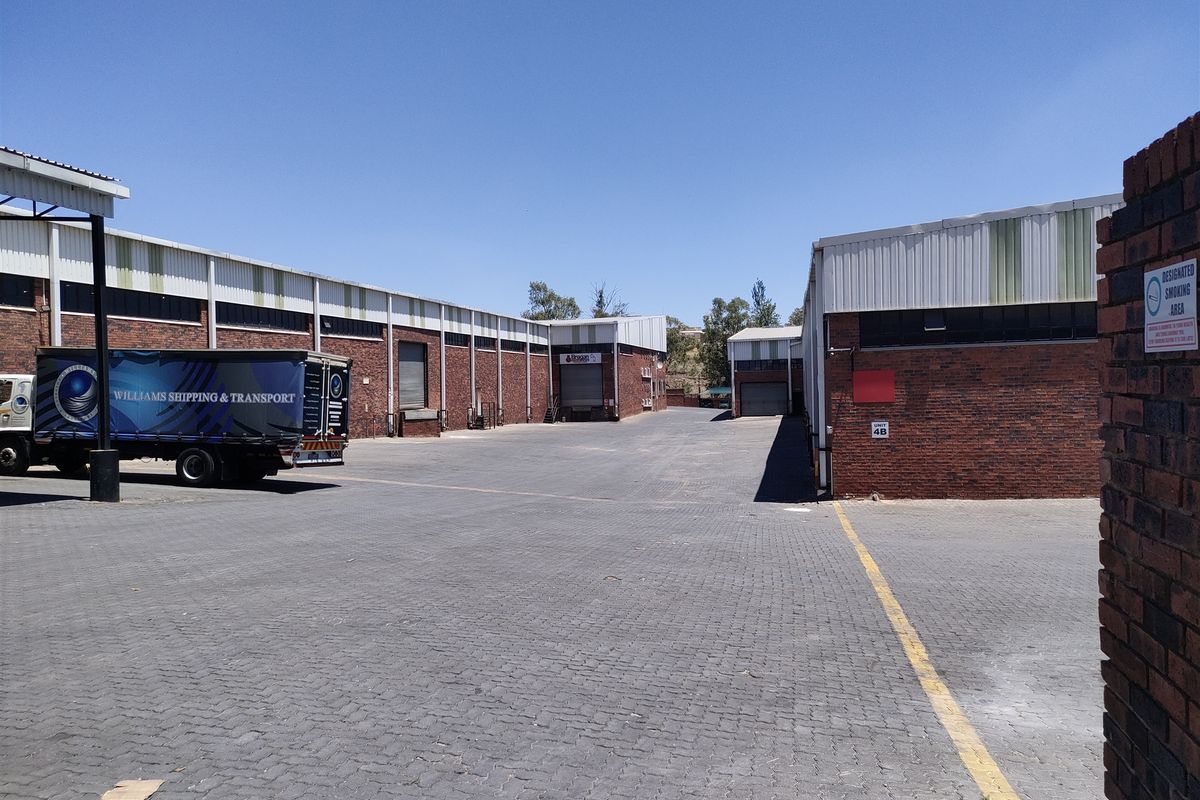 Spacious industrial yard area featuring paved surfaces, multiple roller shutter access points, and brick-clad warehouse structures suitable for logistics and transport operations.