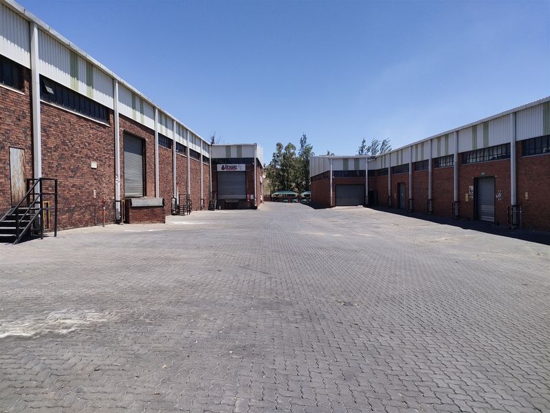 Spacious industrial yard featuring multiple brick warehouse units with roller shutter doors and paved access area.