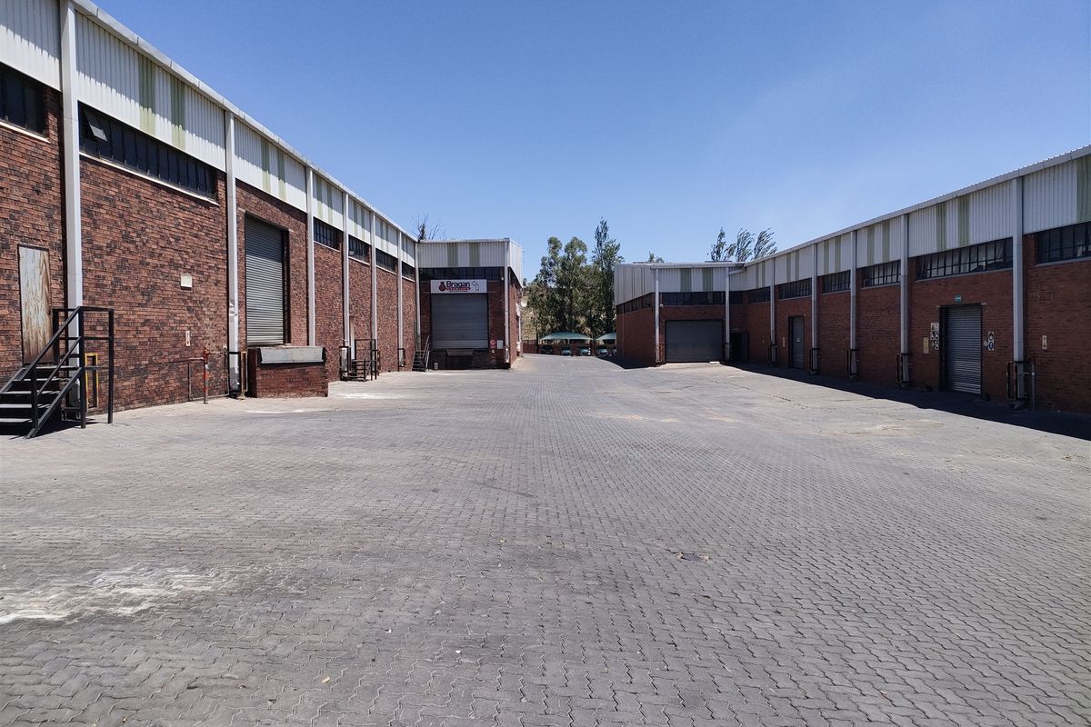 Spacious industrial yard featuring multiple brick warehouse units with roller shutter doors and paved access area.