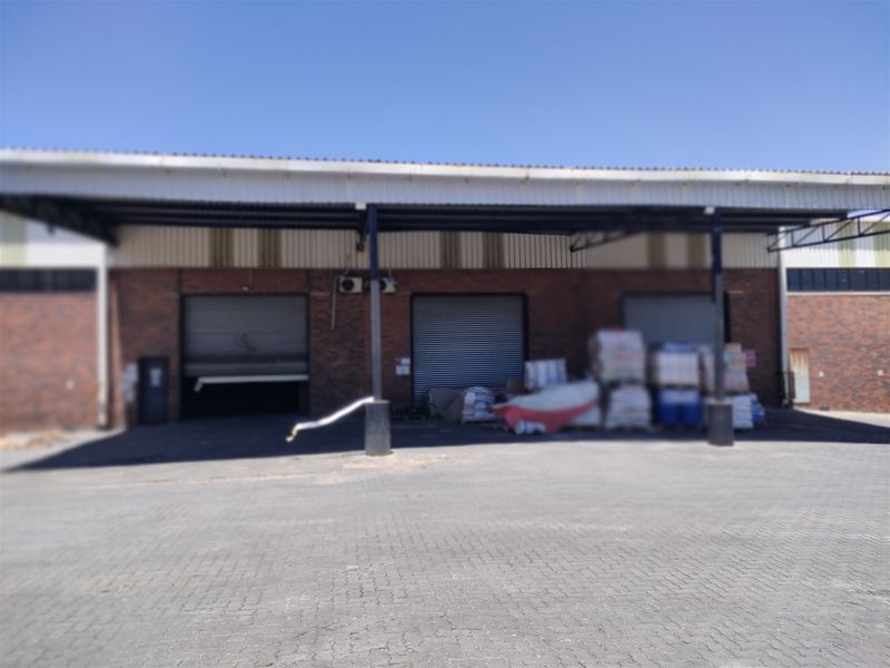 Industrial warehouse exterior featuring multiple roller shutter doors, a covered loading area, and a paved yard space.