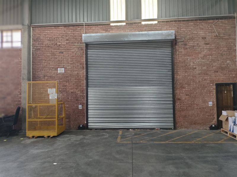 Industrial warehouse interior featuring a large roller shutter door, exposed brickwork, and durable concrete flooring, suitable for logistics or manufacturing operations.