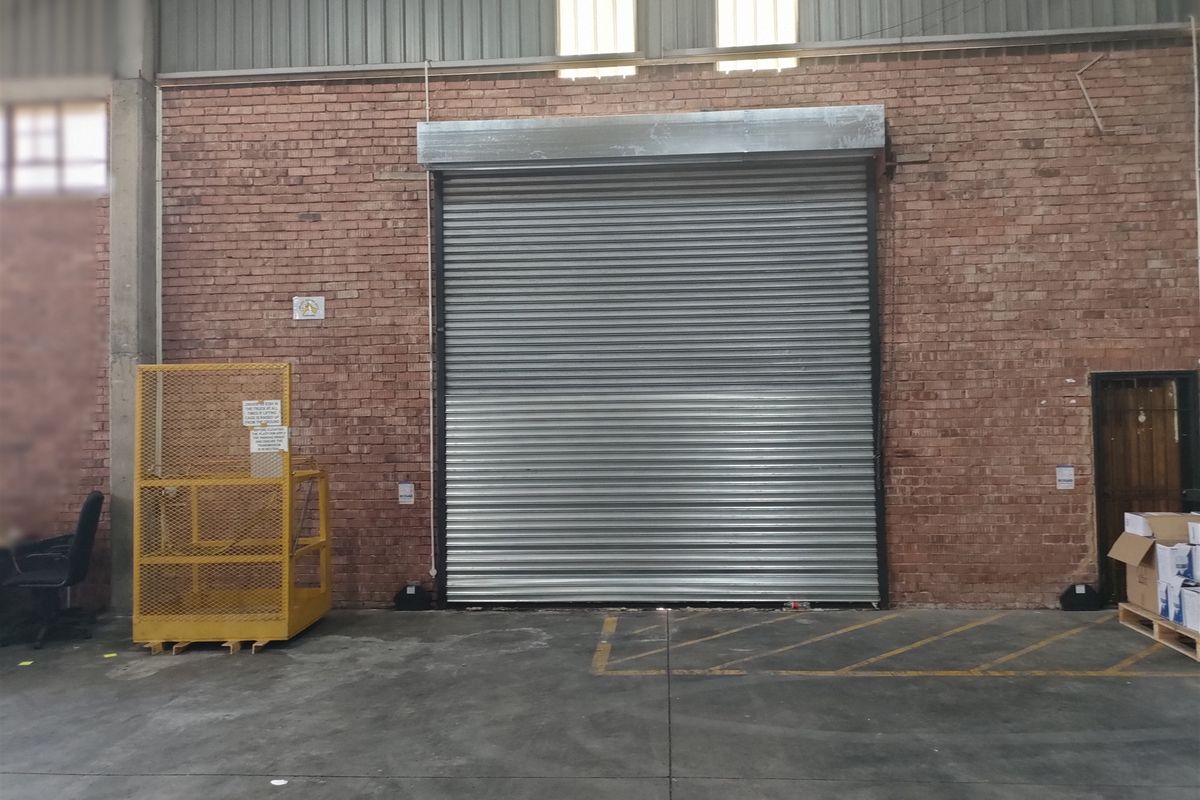 Industrial warehouse interior featuring a large roller shutter door, exposed brickwork, and durable concrete flooring, suitable for logistics or manufacturing operations.