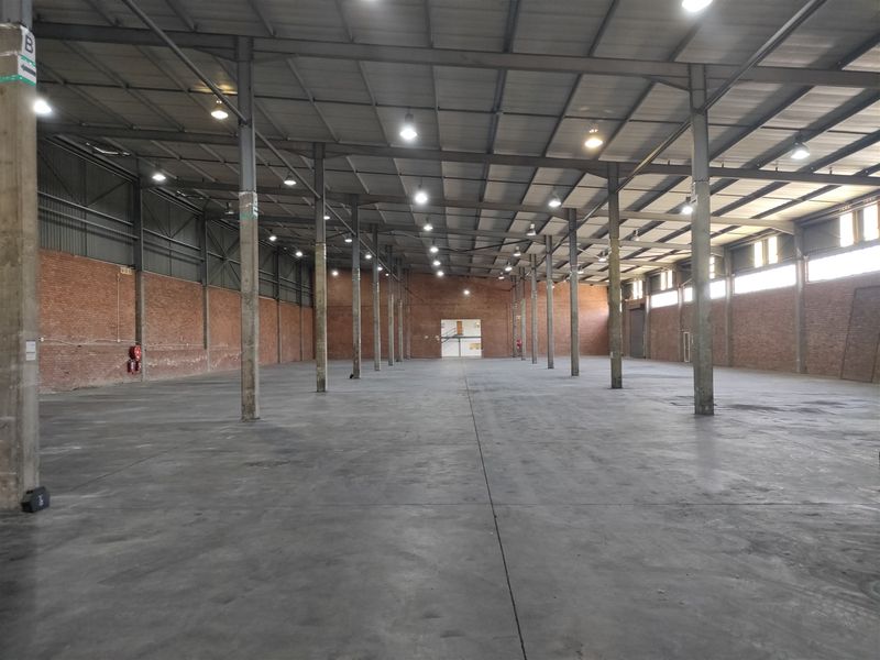 Spacious industrial warehouse featuring high ceilings, exposed steel structural columns, concrete flooring, and brick wall finishes, suitable for storage or manufacturing operations.