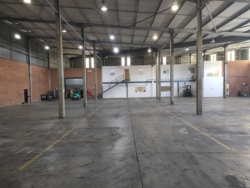 Spacious industrial warehouse featuring high ceilings, exposed steel trusses, concrete flooring, and a mezzanine level with integrated office space.