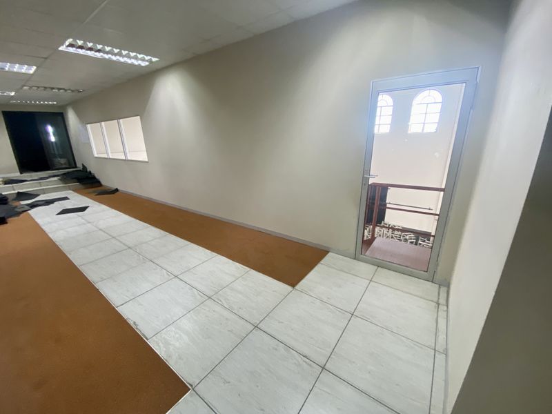A spacious industrial hallway featuring a mix of tiled and carpeted flooring, recessed lighting, and a glass door leading to an adjacent area.