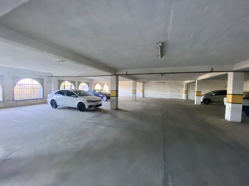 Spacious industrial-style covered parking garage featuring concrete flooring, structural support columns, and arched windows with security grilles.