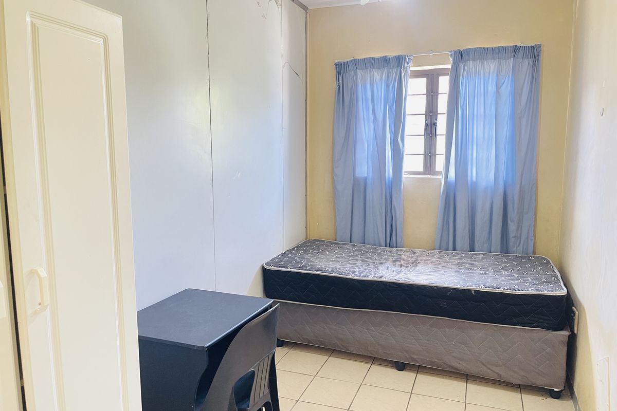 A compact bedroom featuring tiled flooring, a window with security bars, and built-in wall paneling.