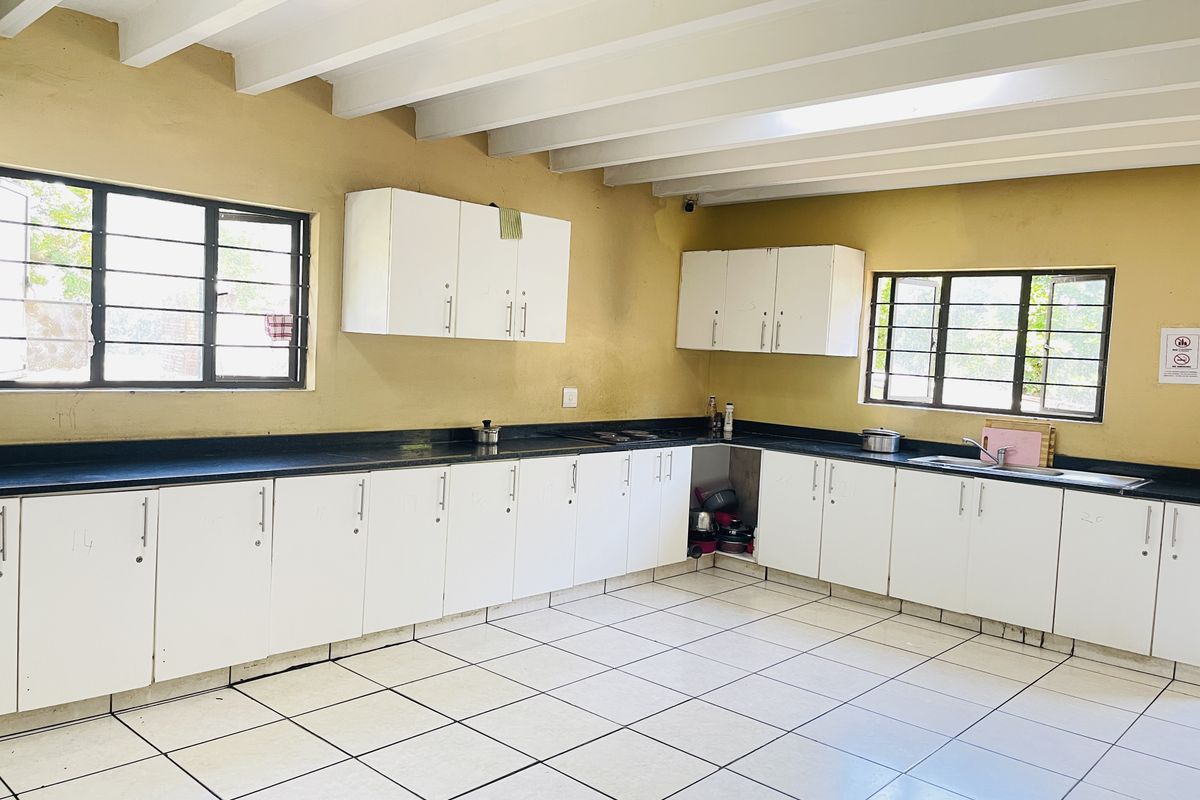 A spacious kitchen featuring white cabinetry, dark countertops, tiled flooring, and exposed beam ceilings, offering ample storage and workspace.