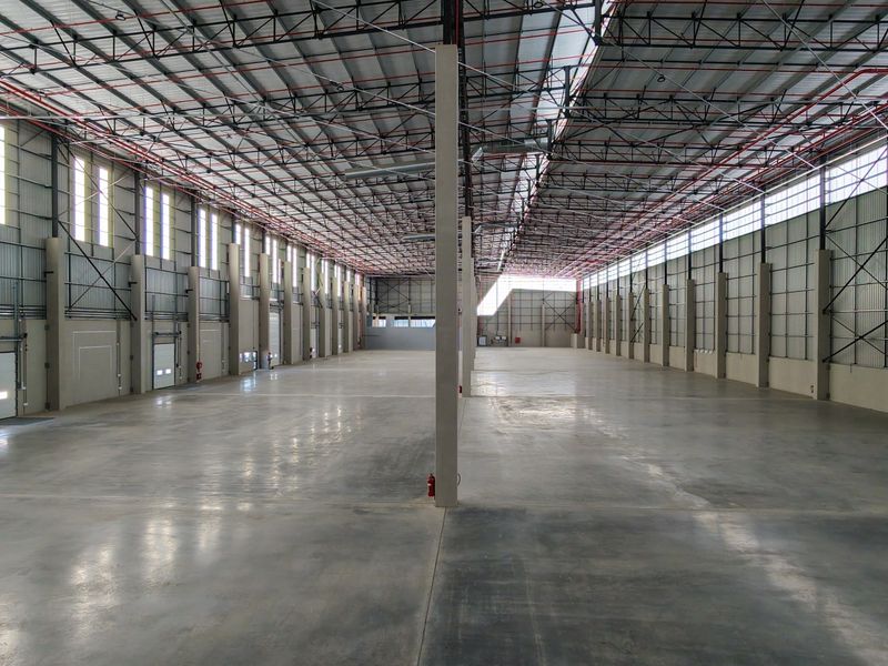 Spacious industrial warehouse featuring high ceilings with exposed steel trusses, polished concrete floors, fire sprinkler systems, and multiple roller shutter access points.