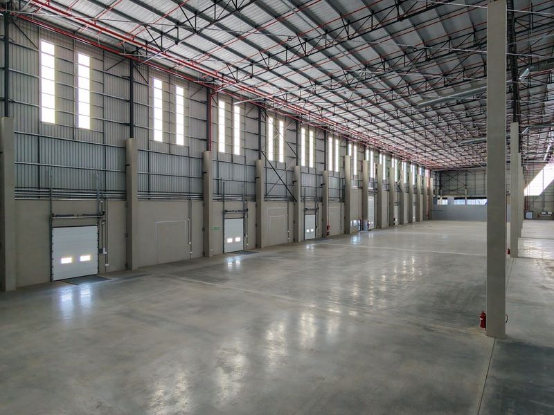 Spacious industrial warehouse featuring polished concrete floors, high-bay windows, multiple roller shutter doors, and an exposed steel portal frame structure with fire sprinkler systems.