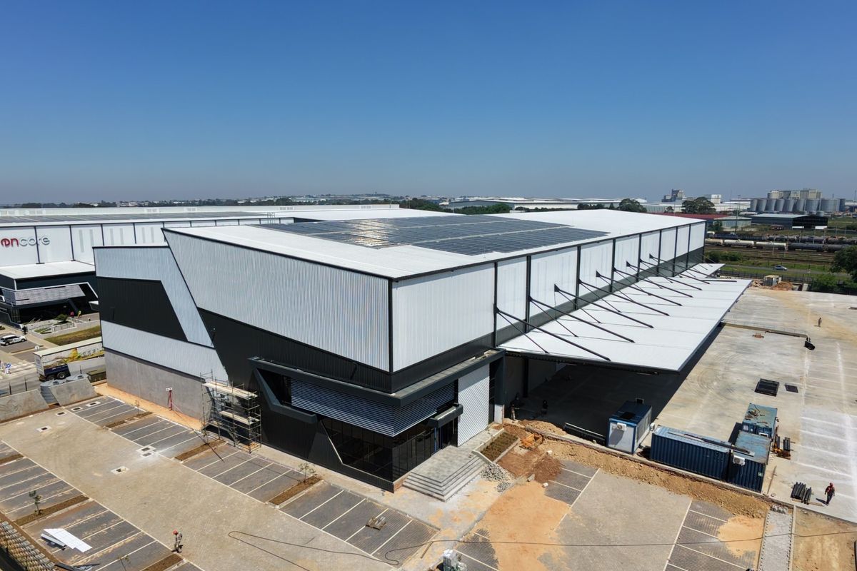 Aerial view of a modern industrial warehouse facility featuring extensive metal cladding, rooftop solar panels, a large loading canopy, and a paved parking area.