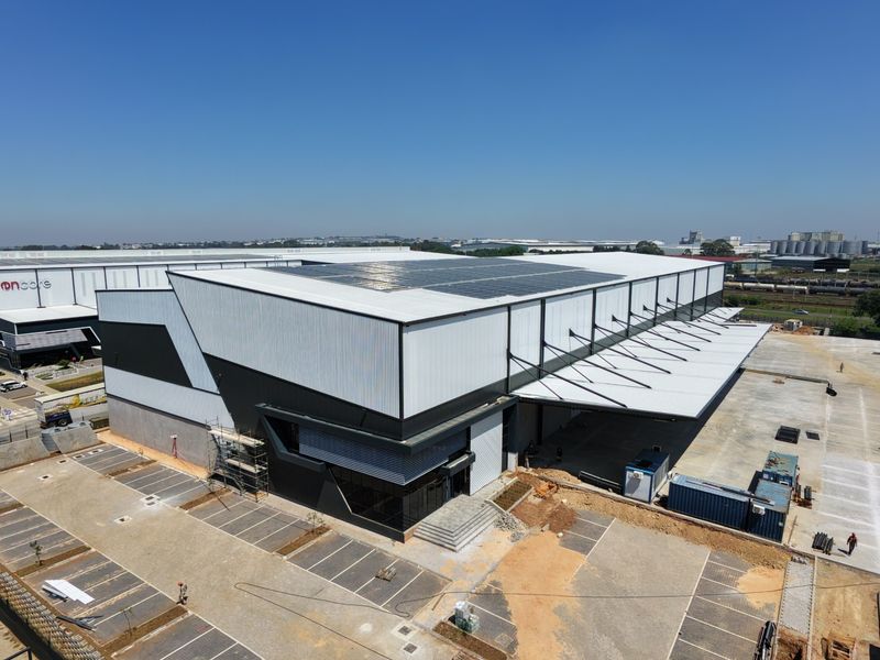 Aerial view of a modern industrial warehouse facility featuring extensive metal cladding, rooftop solar panels, a large loading canopy, and a paved parking area.