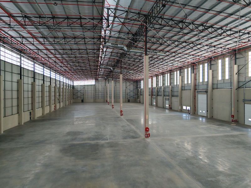 Expansive industrial warehouse space featuring high ceilings with exposed steel trusses, polished concrete flooring, and multiple roller shutter doors for efficient logistics access.