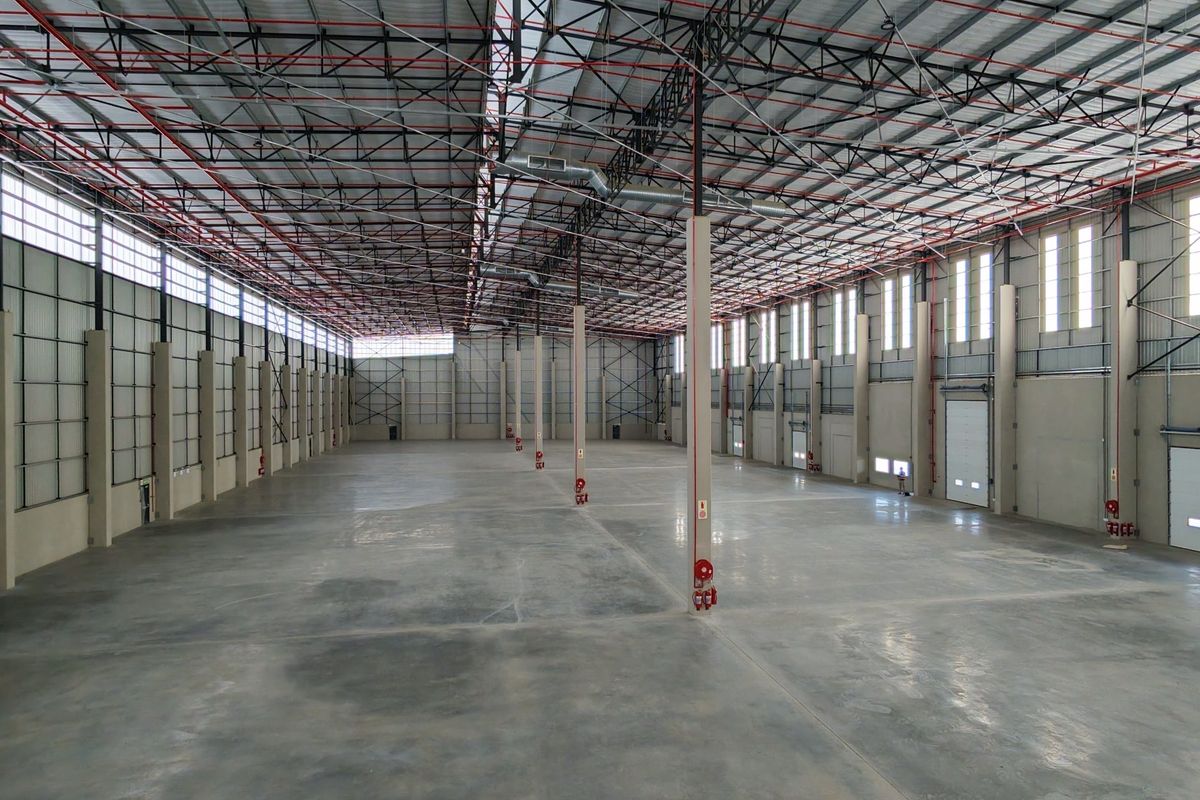 Expansive industrial warehouse space featuring high ceilings with exposed steel trusses, polished concrete flooring, and multiple roller shutter doors for efficient logistics access.