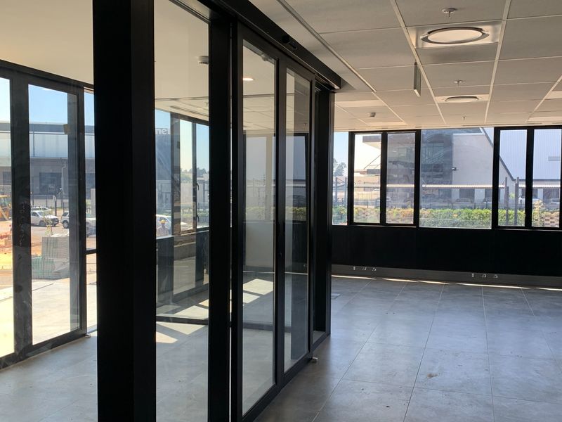Modern, open-plan office space featuring large glass windows, aluminium partitions, tiled flooring, and a suspended ceiling with recessed lighting.