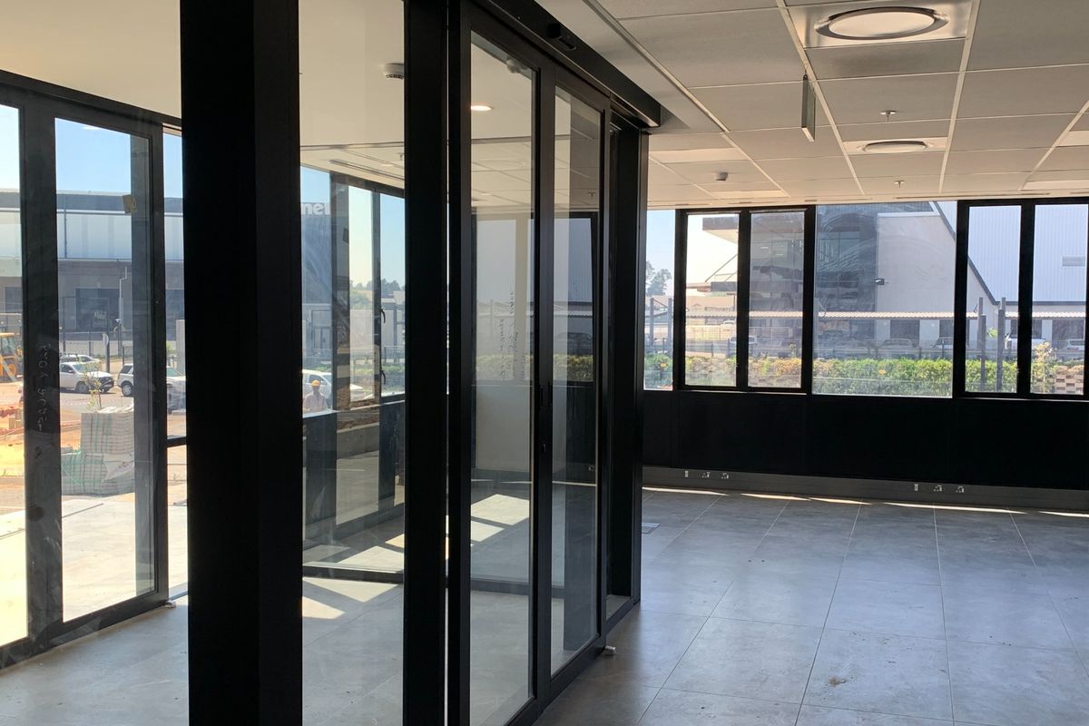 Modern, open-plan office space featuring large glass windows, aluminium partitions, tiled flooring, and a suspended ceiling with recessed lighting.