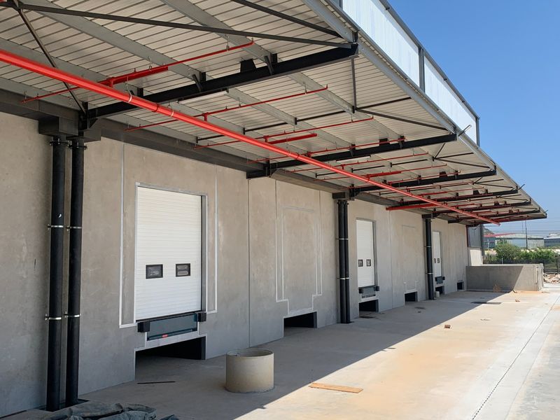 Industrial loading bay area featuring multiple roller shutter doors, overhead fire sprinkler system, and a concrete loading apron.