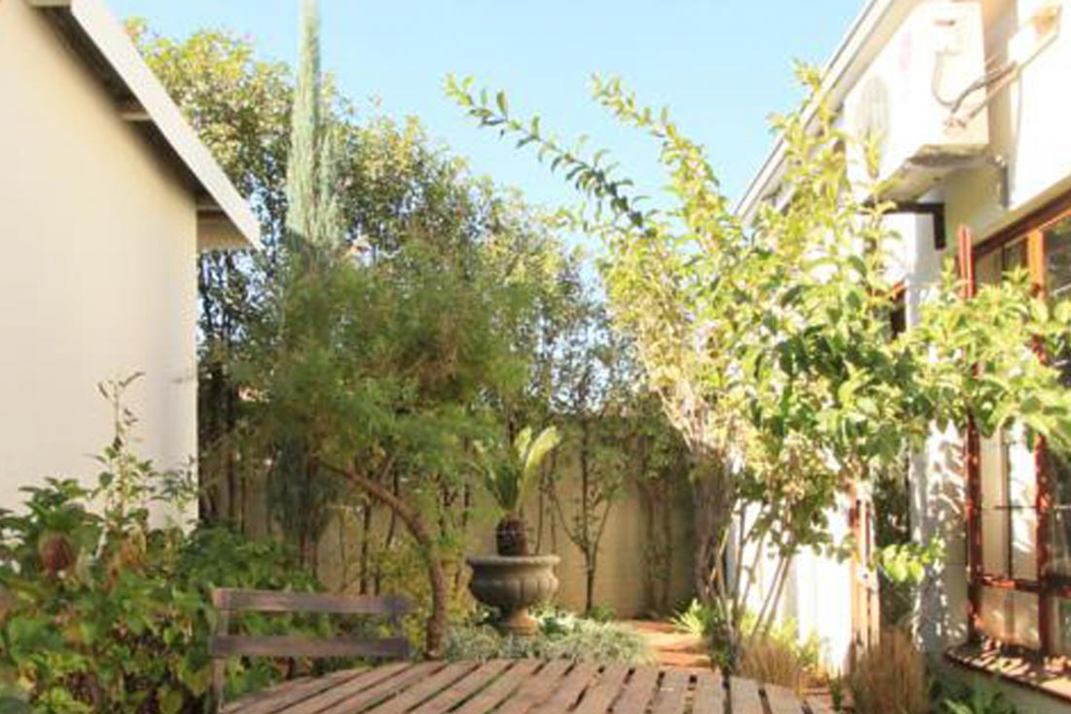A private rear courtyard garden featuring established greenery, wall-mounted exterior lighting, and an air conditioning unit installed on the building facade.