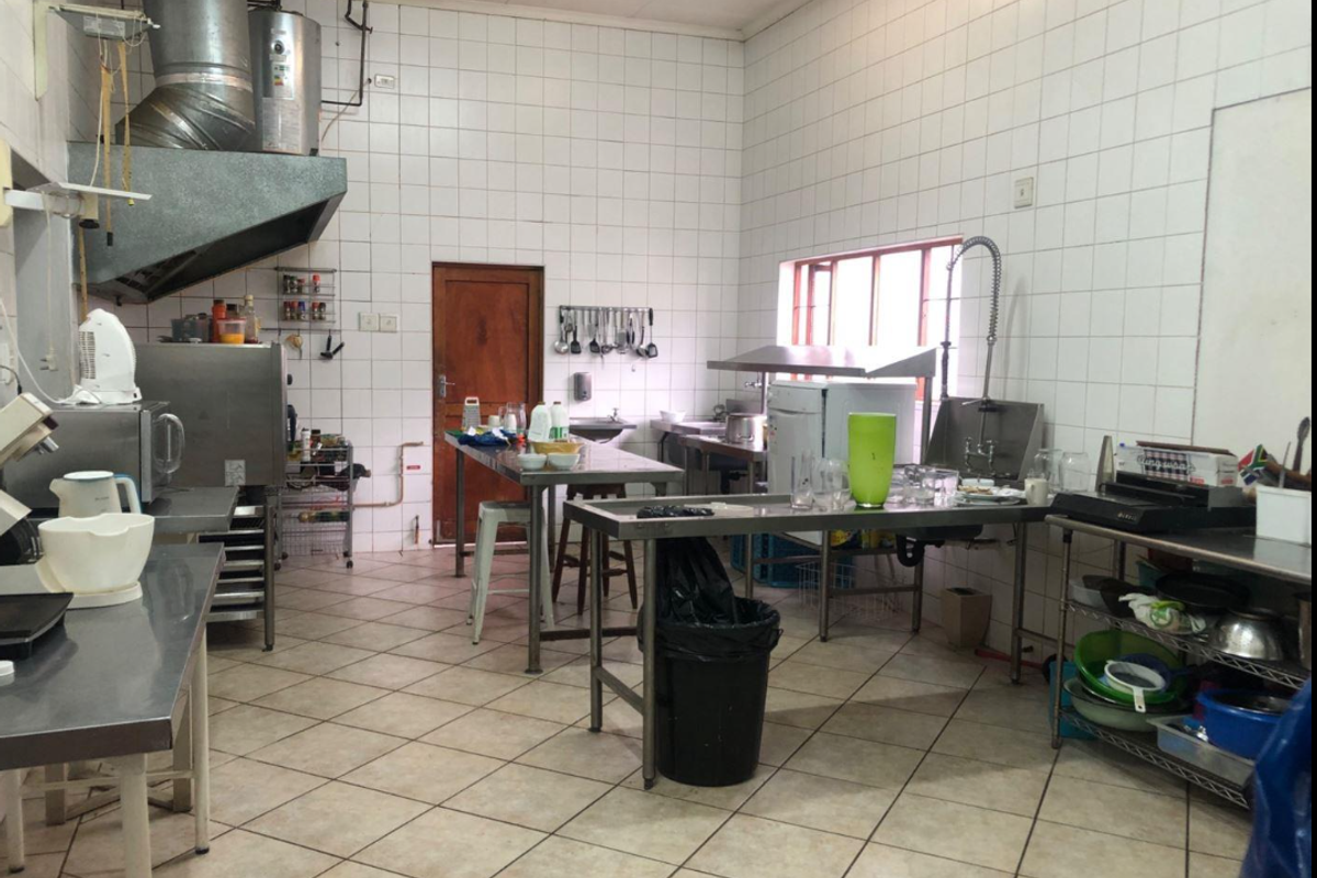 A functional commercial-style kitchen featuring stainless steel prep surfaces, tiled walls, and industrial-grade extraction equipment, suitable for high-volume food preparation.