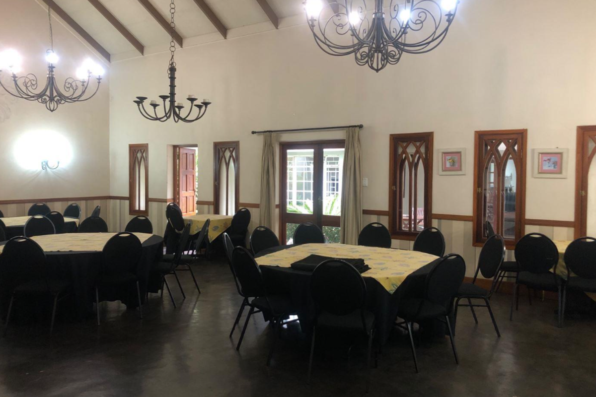 Spacious dining or event hall featuring a high vaulted ceiling with exposed timber beams, polished concrete floors, and distinctive gothic-style arched windows.
