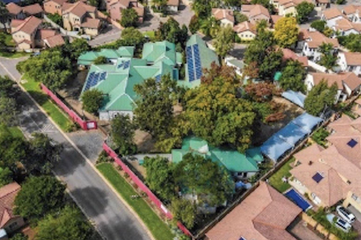 Aerial view of the property showcasing the building layout, green pitched roof, and installed solar panels within a residential estate setting.