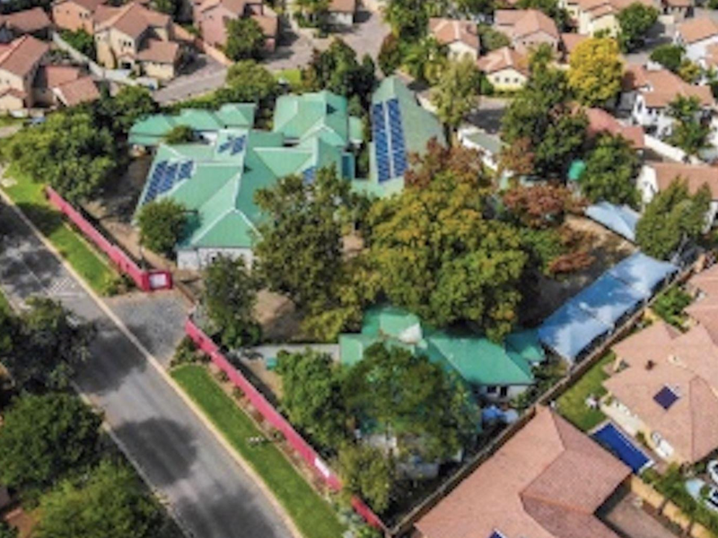 Aerial view of the property showcasing the building layout, green pitched roof, and installed solar panels within a residential estate setting.