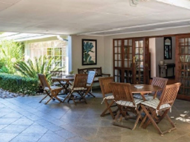 A spacious covered patio featuring tiled flooring and wooden french doors, providing seamless access to the lush landscaped garden area.