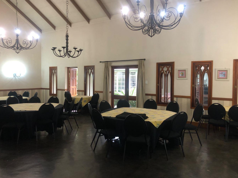Spacious dining or event hall featuring a high vaulted ceiling with exposed timber beams, polished concrete floors, and distinctive gothic-style arched windows.