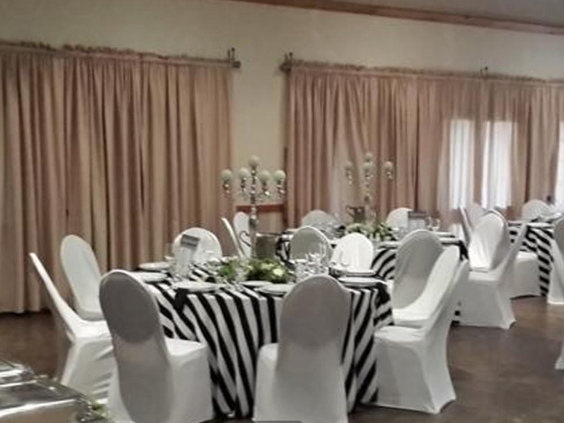 A spacious event hall or clubhouse area featuring tiled flooring, neutral wall finishes, and large windows covered by floor-to-ceiling curtains.