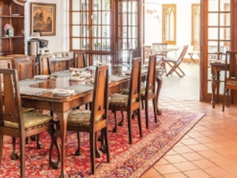A spacious dining room featuring traditional terracotta tile flooring, built-in wooden cabinetry, and large wooden french doors opening to an outdoor patio area.