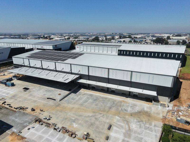 Aerial view of a large industrial warehouse facility featuring extensive solar panel installations, multiple loading bays, and a spacious concrete yard.