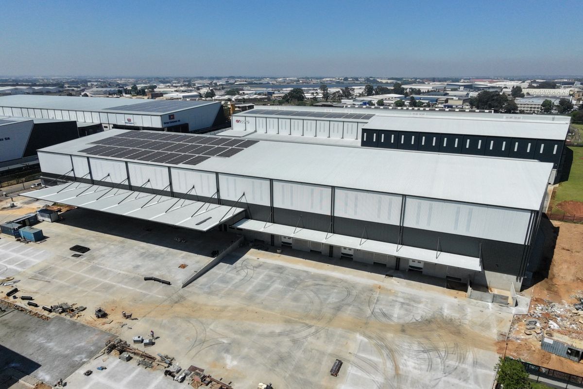 Aerial view of a large industrial warehouse facility featuring extensive solar panel installations, multiple loading bays, and a spacious concrete yard.