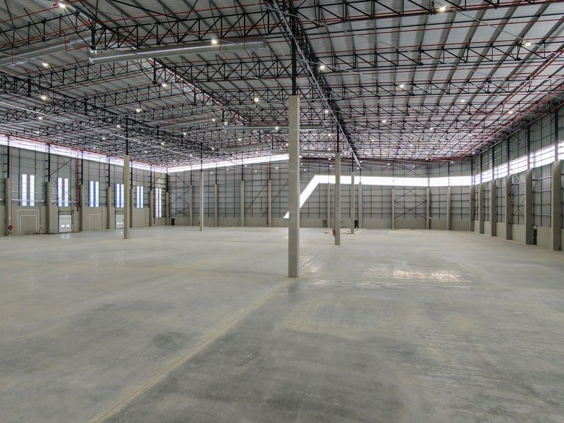 Spacious industrial warehouse featuring high ceilings with exposed steel trusses, polished concrete flooring, and ample natural light through clerestory windows.