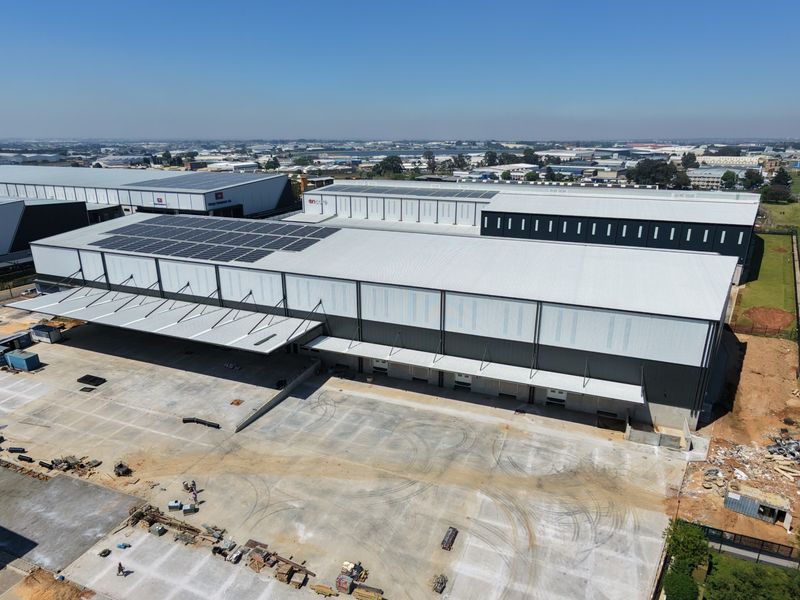 Aerial view of a large industrial warehouse facility featuring extensive solar panel installations, multiple loading bays, and a spacious concrete yard.