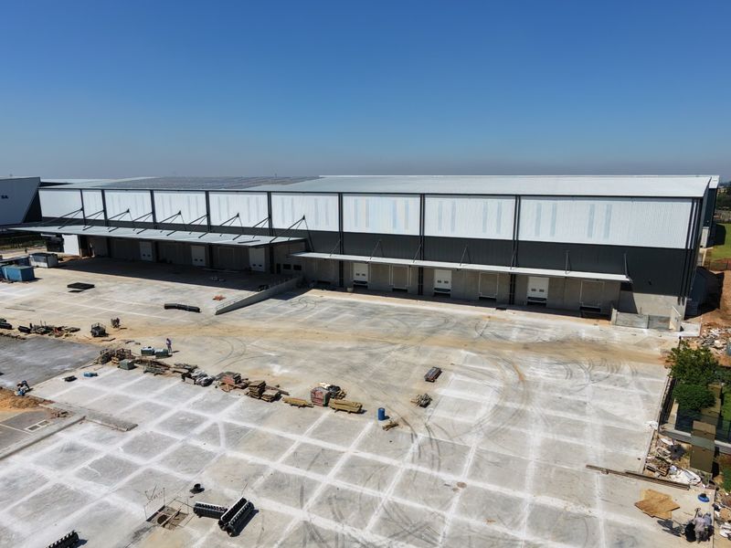 Aerial view of a large industrial warehouse facility featuring multiple loading docks, extensive concrete hardstand area, and roof-mounted solar panels.